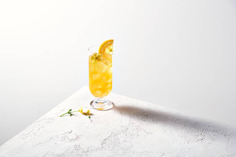 Nona June Minona alkoholfrei: Auf einem Marmortisch steht ein Cocktailglas mit einem Longdrink und einer Orangenscheibe.