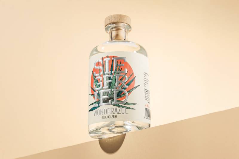 Wonderazul alkoholfrei in einer stylischen Flasche mit der Aufschrift "Siegfried". Im Hintergrund sieht man eine Sonne und eine Agave.