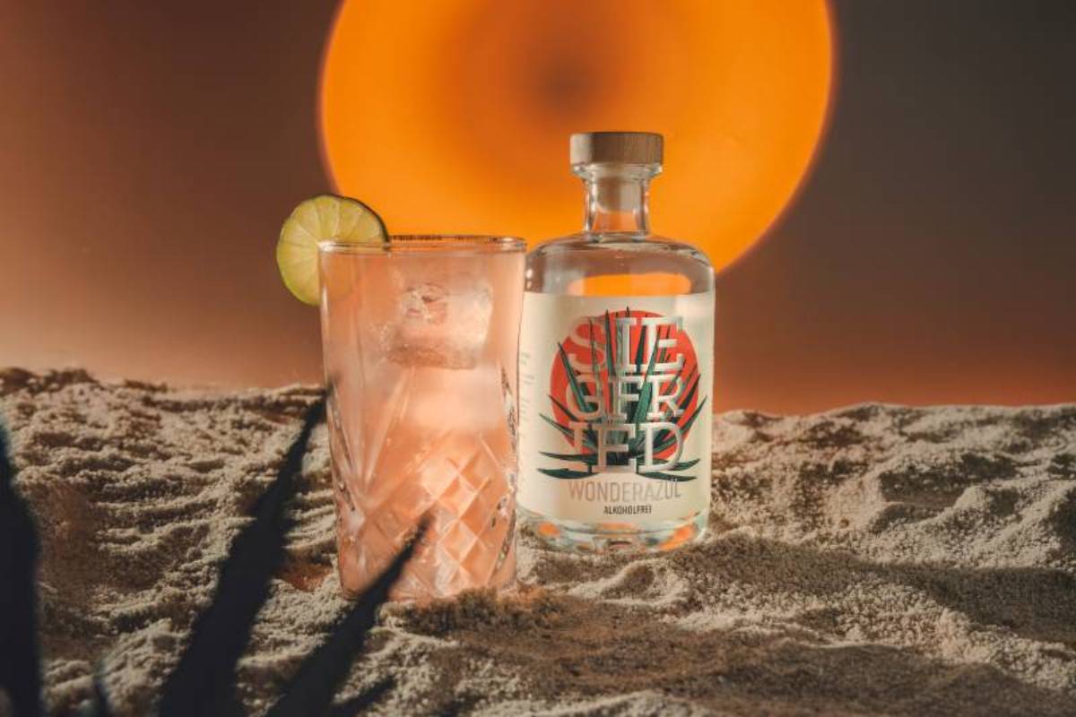 Wonderazul alkoholfrei in einer stylischen Flasche mit der Aufschrift "Siegfried" neben einem Glas mit Eiswürfeln und einer Limettenscheibe.