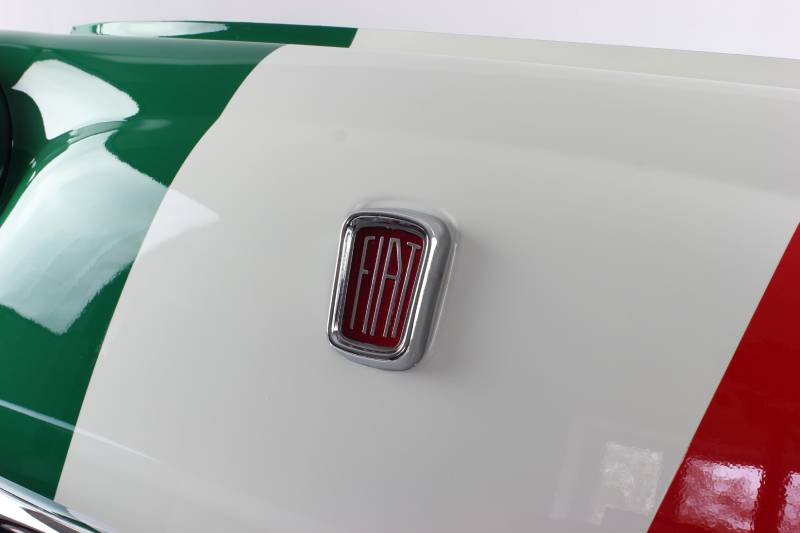 Es ist eine Großaufnahme der dreifarbigen Motorhaube eines Fiat (grün, weiß, rot) mit dem Fiat-Emblem in der Mitte zu sehen.